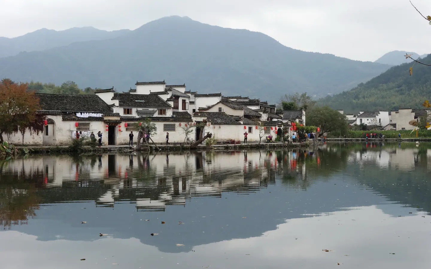 山水背景下南湖沿岸白墙黛瓦聚落连片分布，居民与来访者行走在湖岸