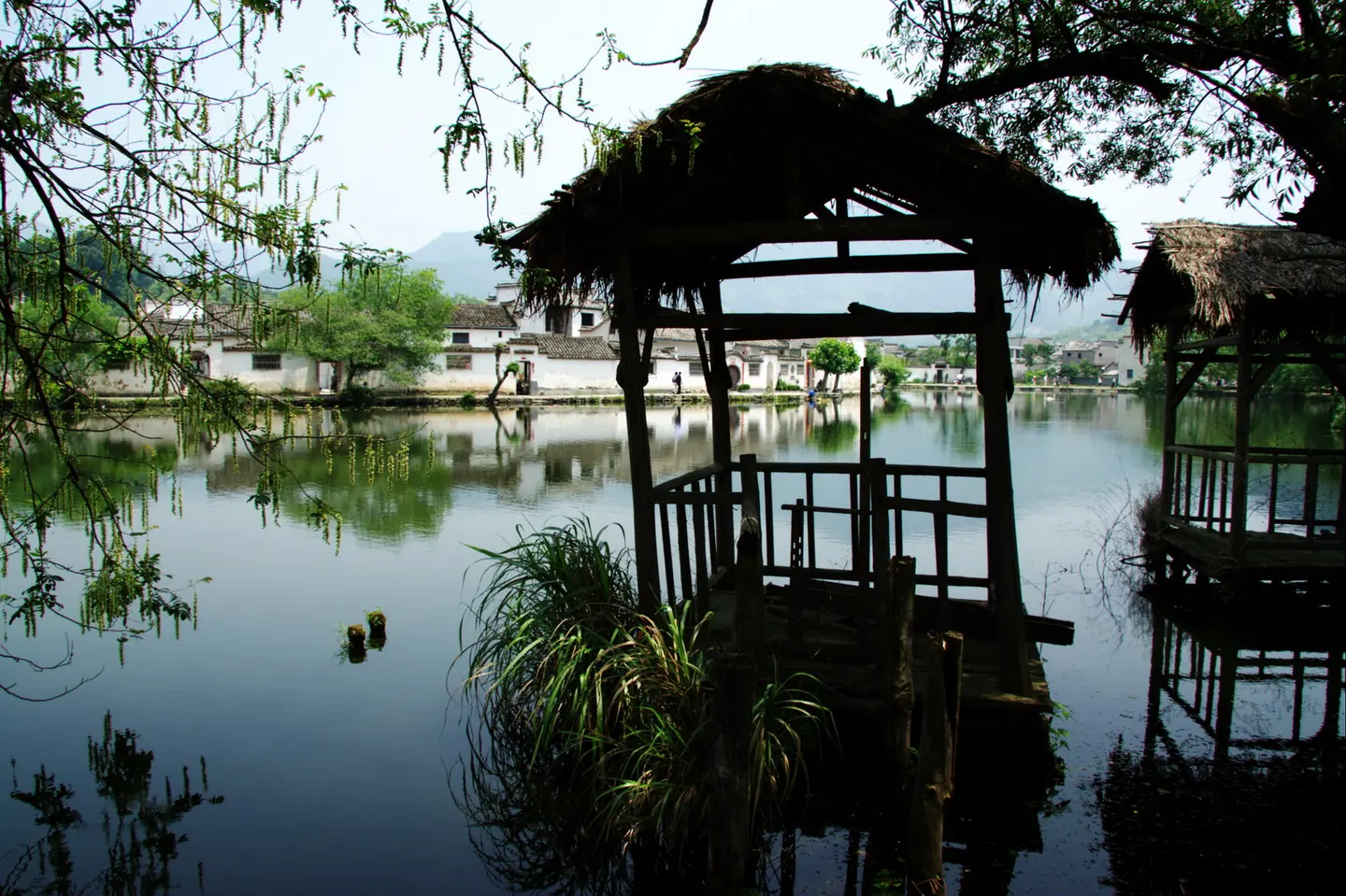 南湖岸边两座草亭临水而立，对岸白墙民居与树影映入水面